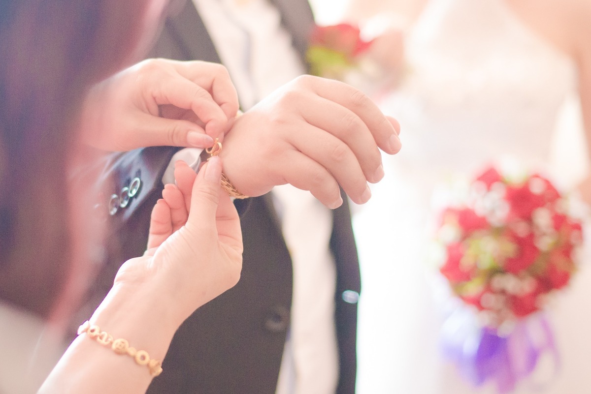 Mãos femininas fechando pulseira dourada em volta de pulso masculino.