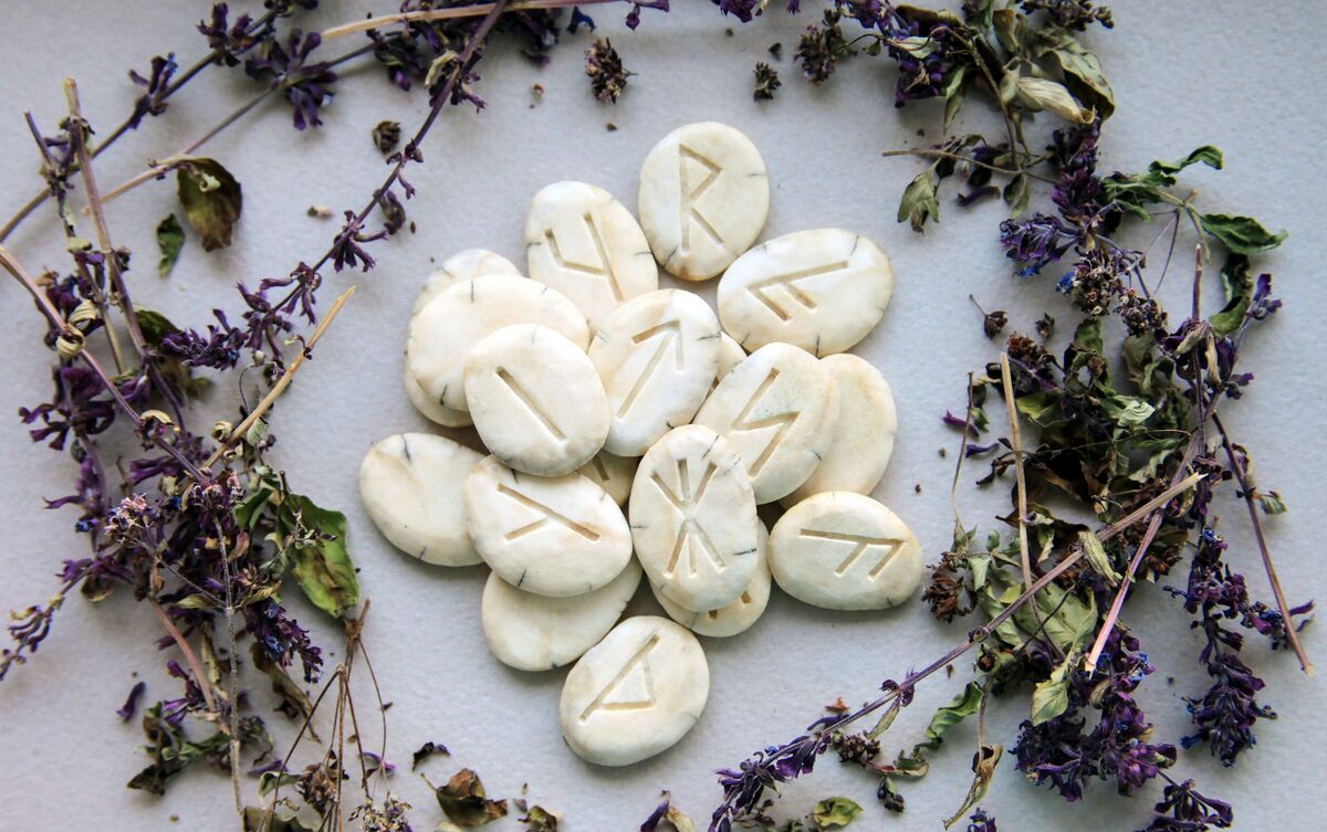 Pedras de runas com flores roxas ao redor.