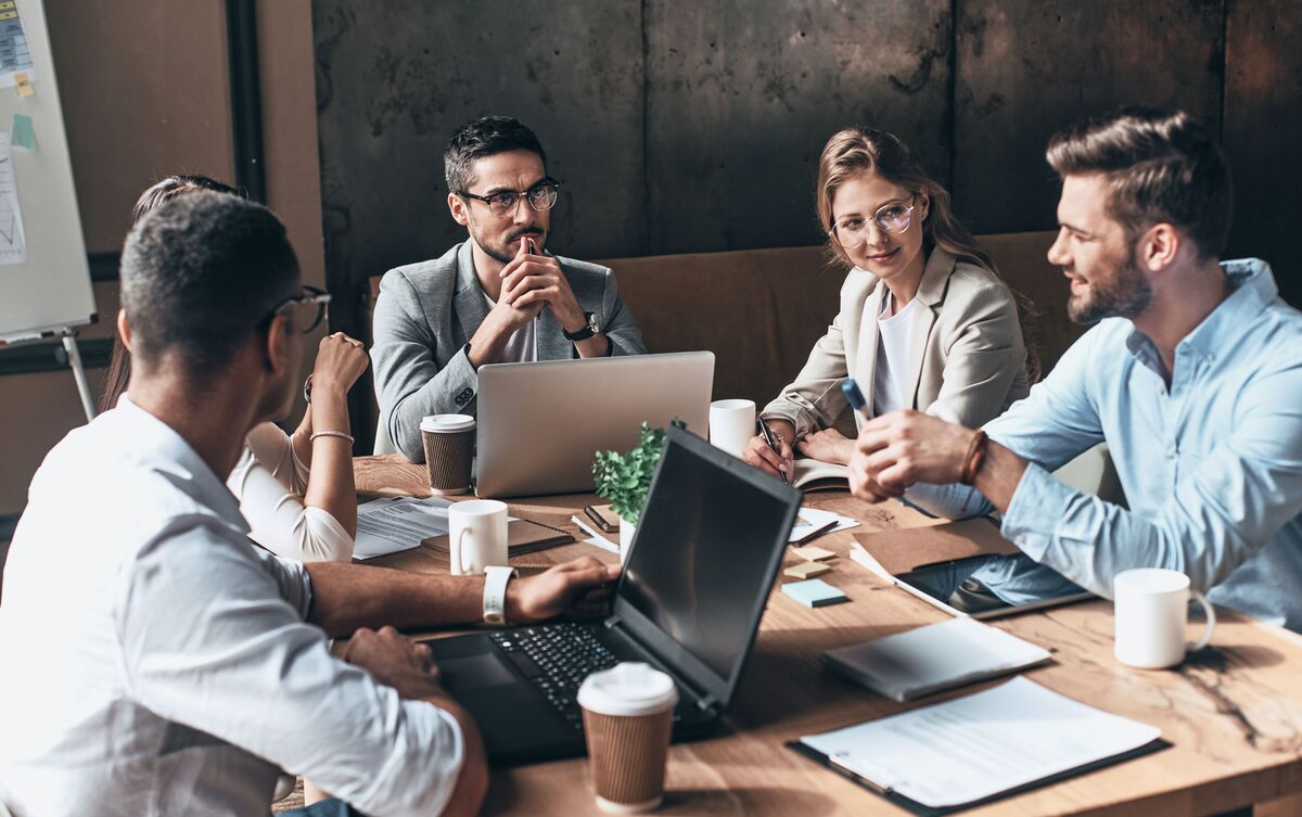 Grupo de pessoas em volta de mesa em ambiente de trabalho.