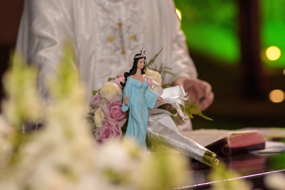 Pequena estátua de Iemanjá ao lado de sacerdote, em meio à celebração.