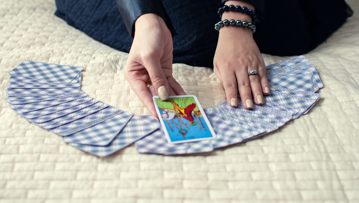 Mão tirando carta de baralho de Tarot espalhado em cima da cama. 