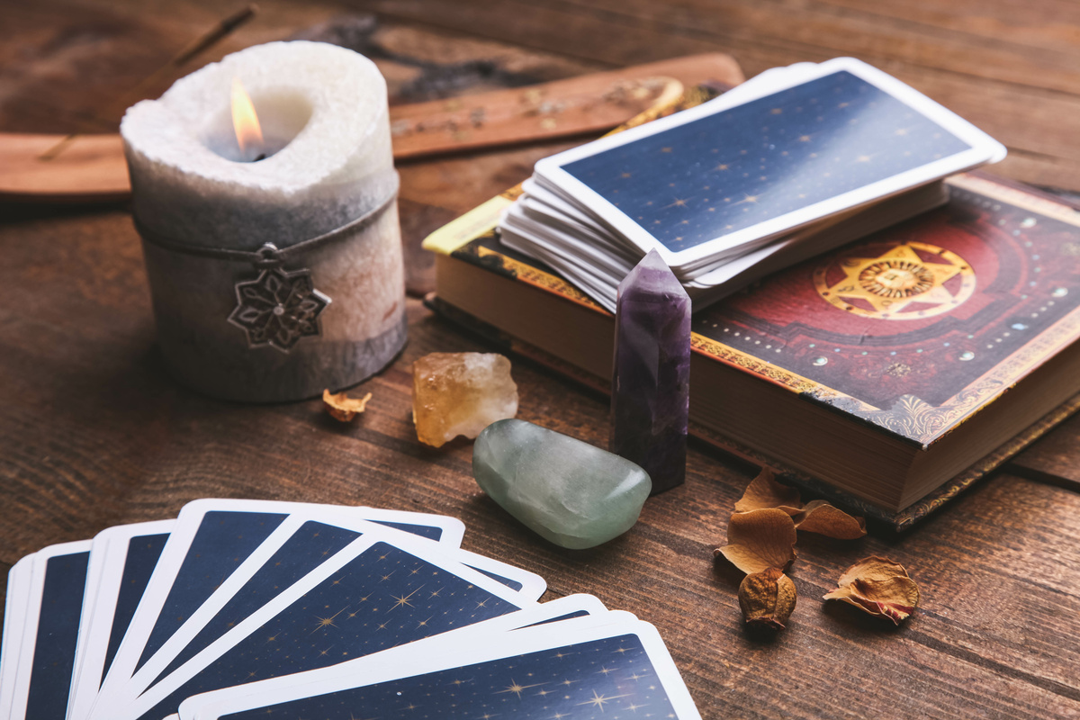 Cartas de Tarot azuis enfileiradas e em cima de livro, ao lado de velas e cristais.