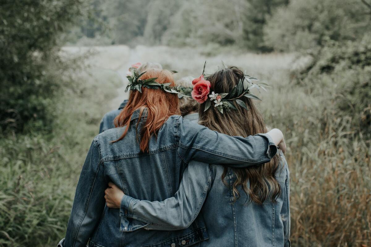 Duas mulheres abraçadas, com coroas de flores, em um campo gramado.