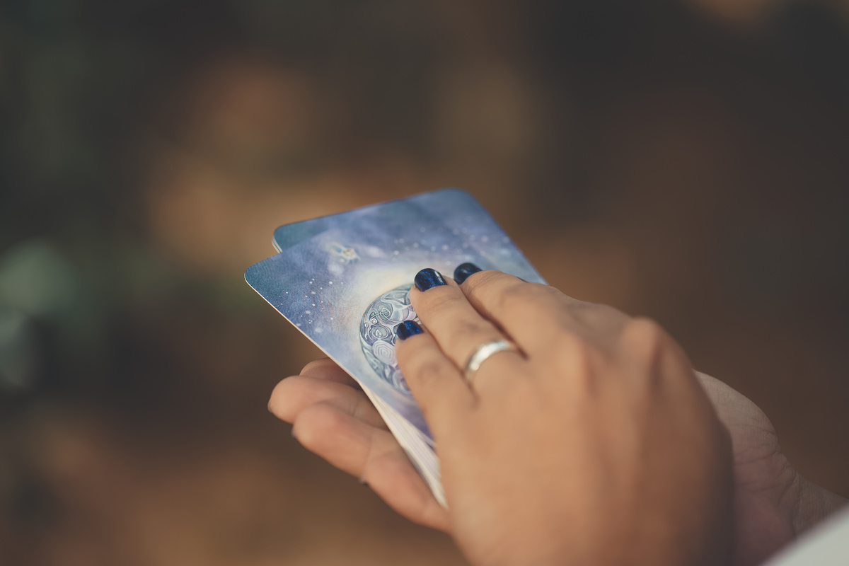 Mãos com unhas pintadas segurando baralho de Tarot azul em suas mãos.