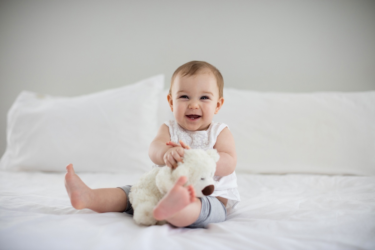 Bebê brincando com ursinho em cima da cama