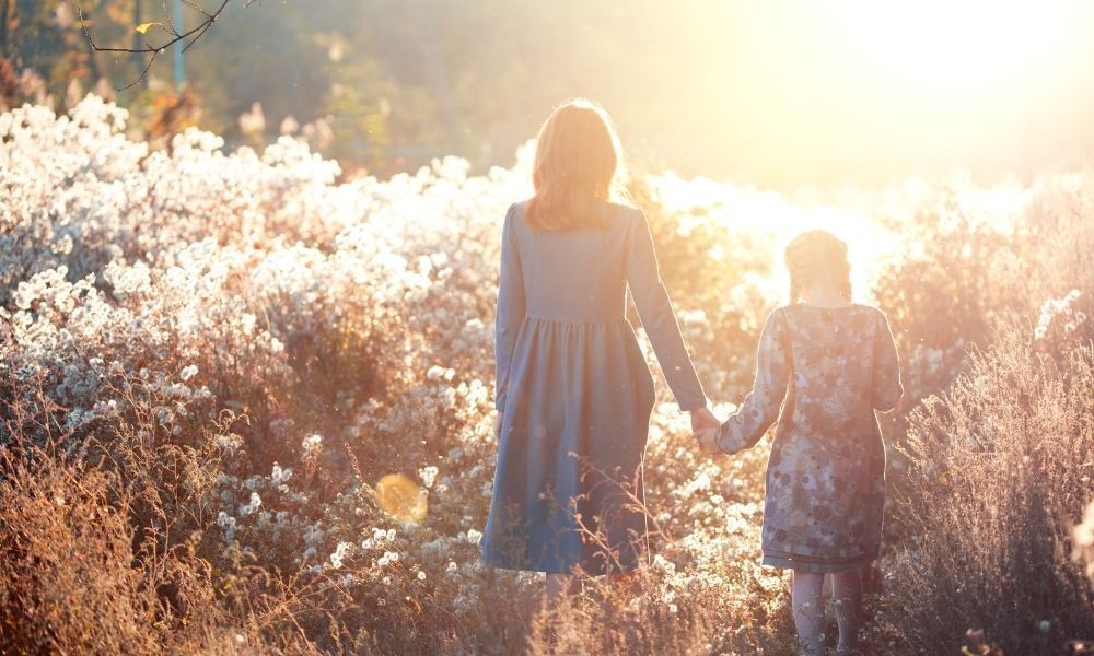 Uma mãe e sua filha caminham em um campo no entardecer. 