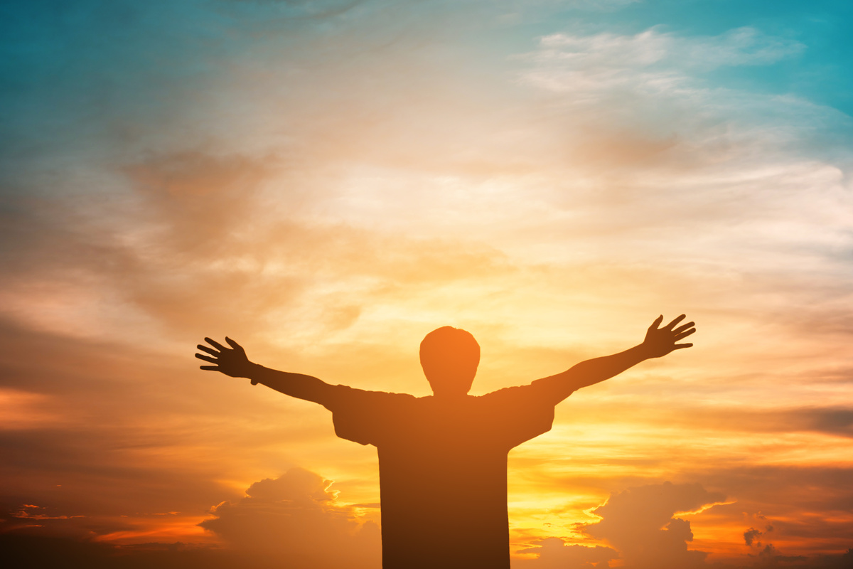 Homem com braços abertos olhando para o Sol