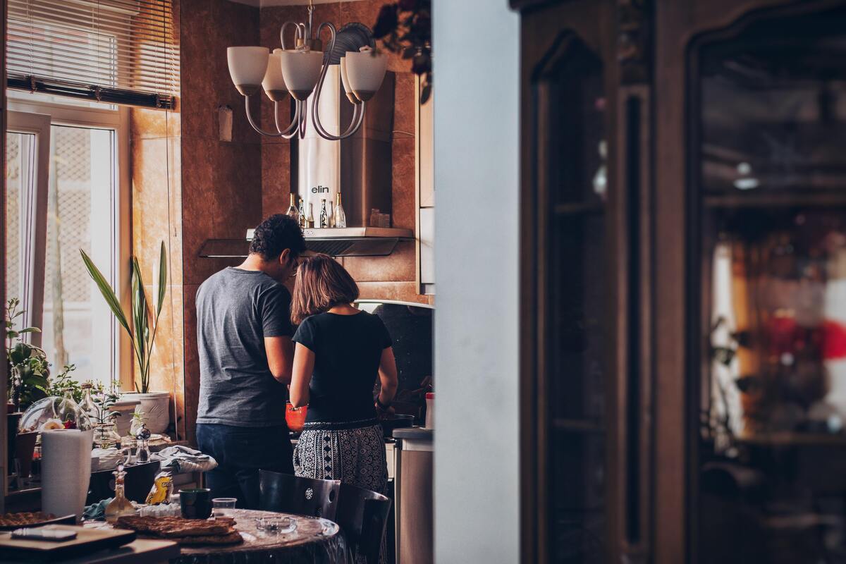 Casal em pé dentro de uma cozinha.