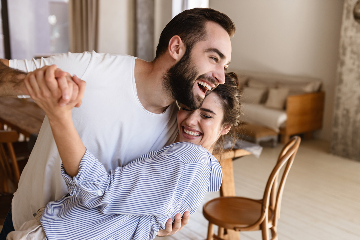 Casal rindo e dançando na sala de uma casa