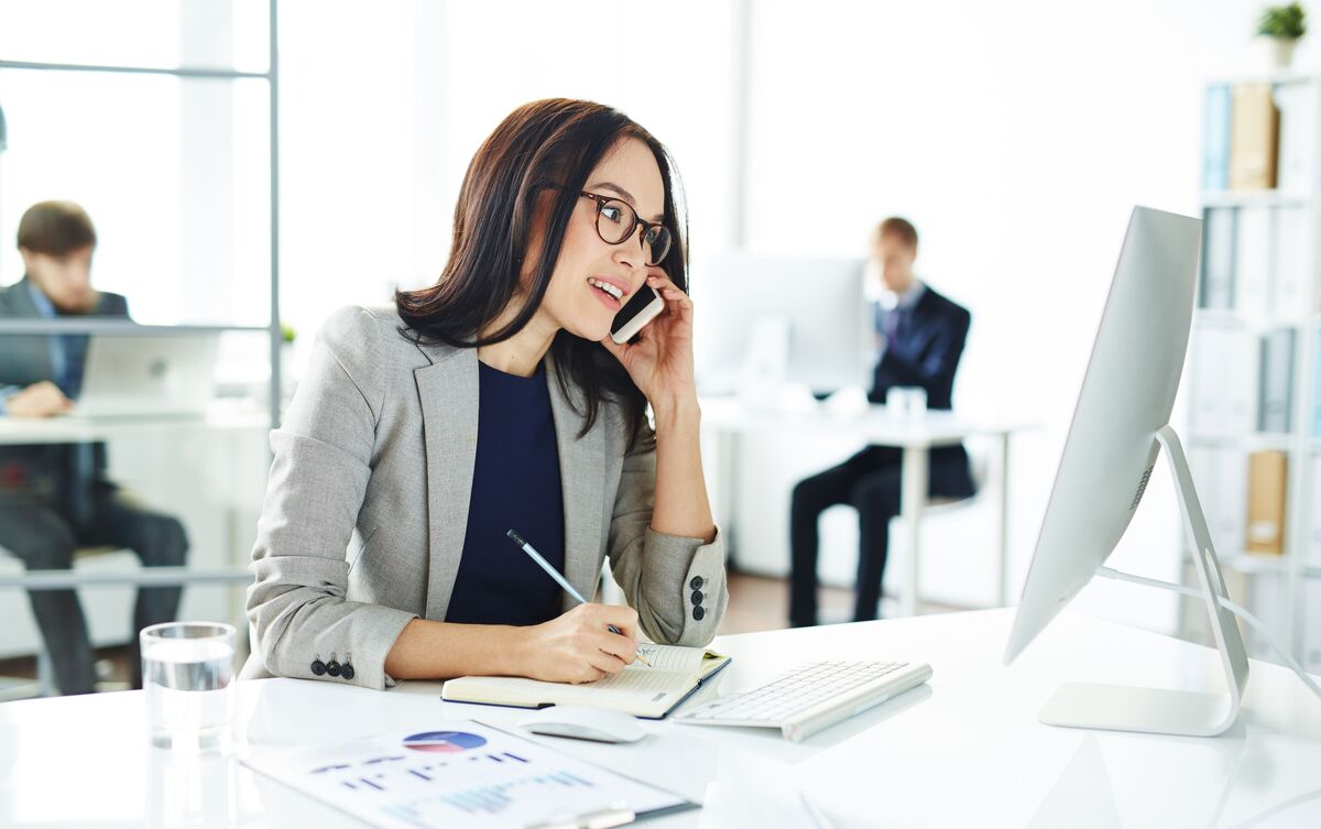 Mulher sentada em ambiente de trabalho falando ao telefone.