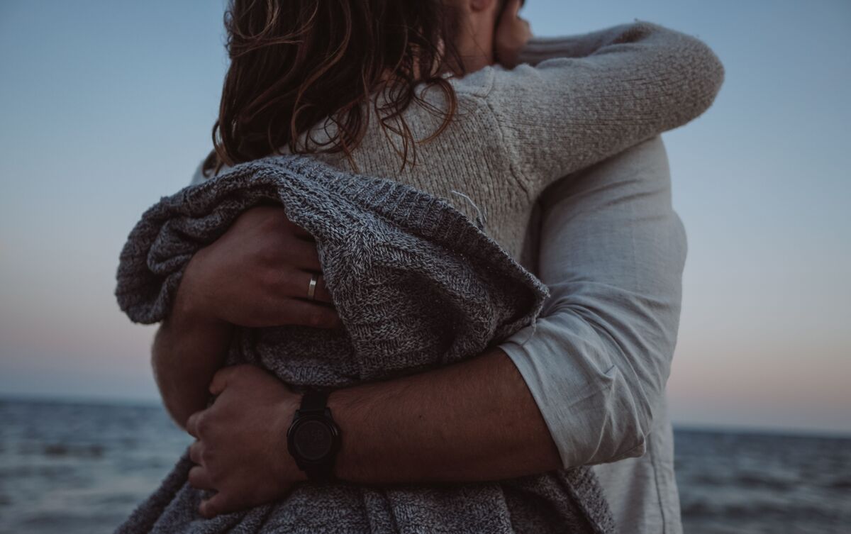 Homem e mulher abraçados em praia.