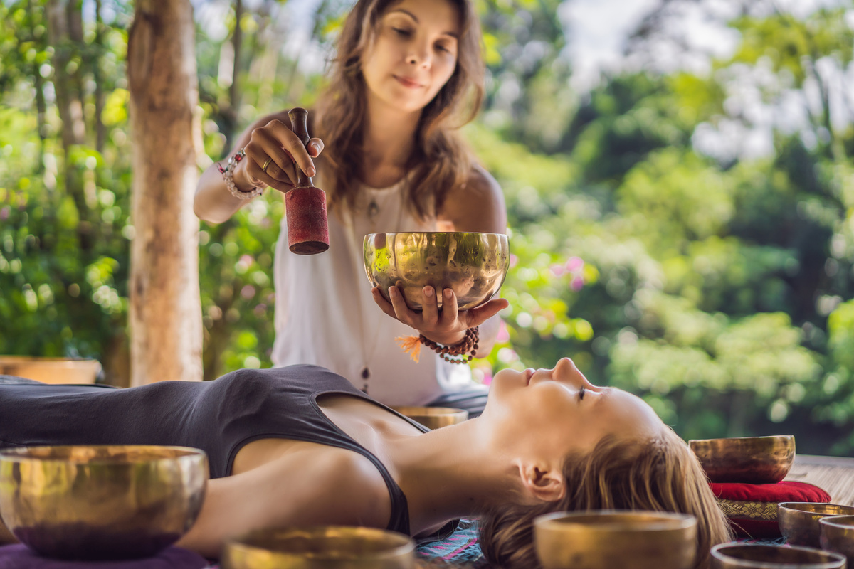 Uma mulher com objetos nas mãos realizando terapia em outra mulher deitada