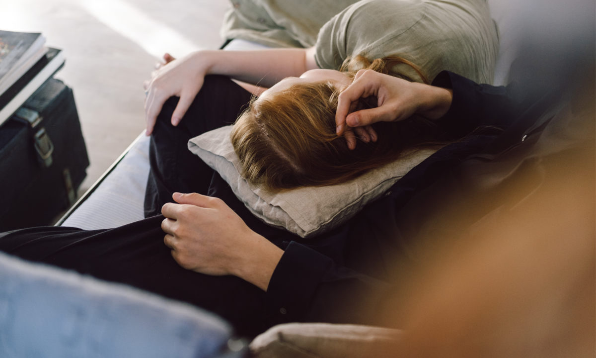 Mulher deitada no colo de um homem, enquanto ele faz carinho na cabeça dela. 