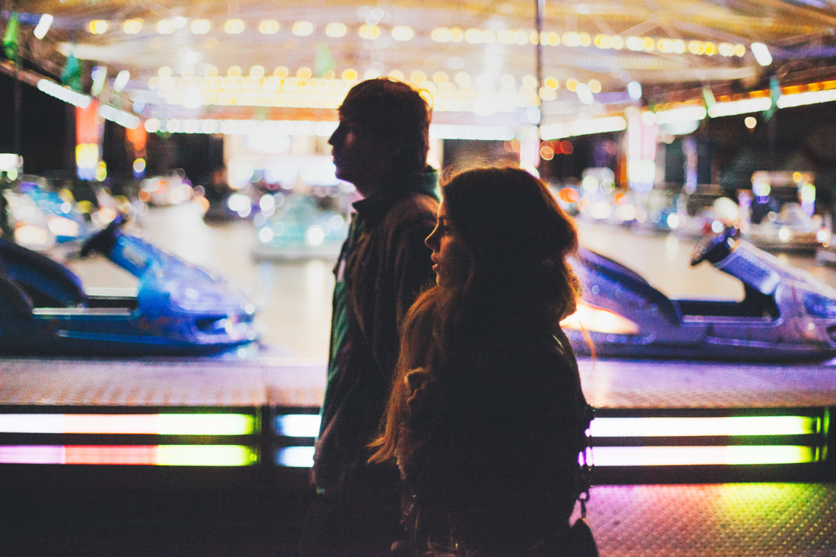 Casal andando lado a lado em um parque de diversões.