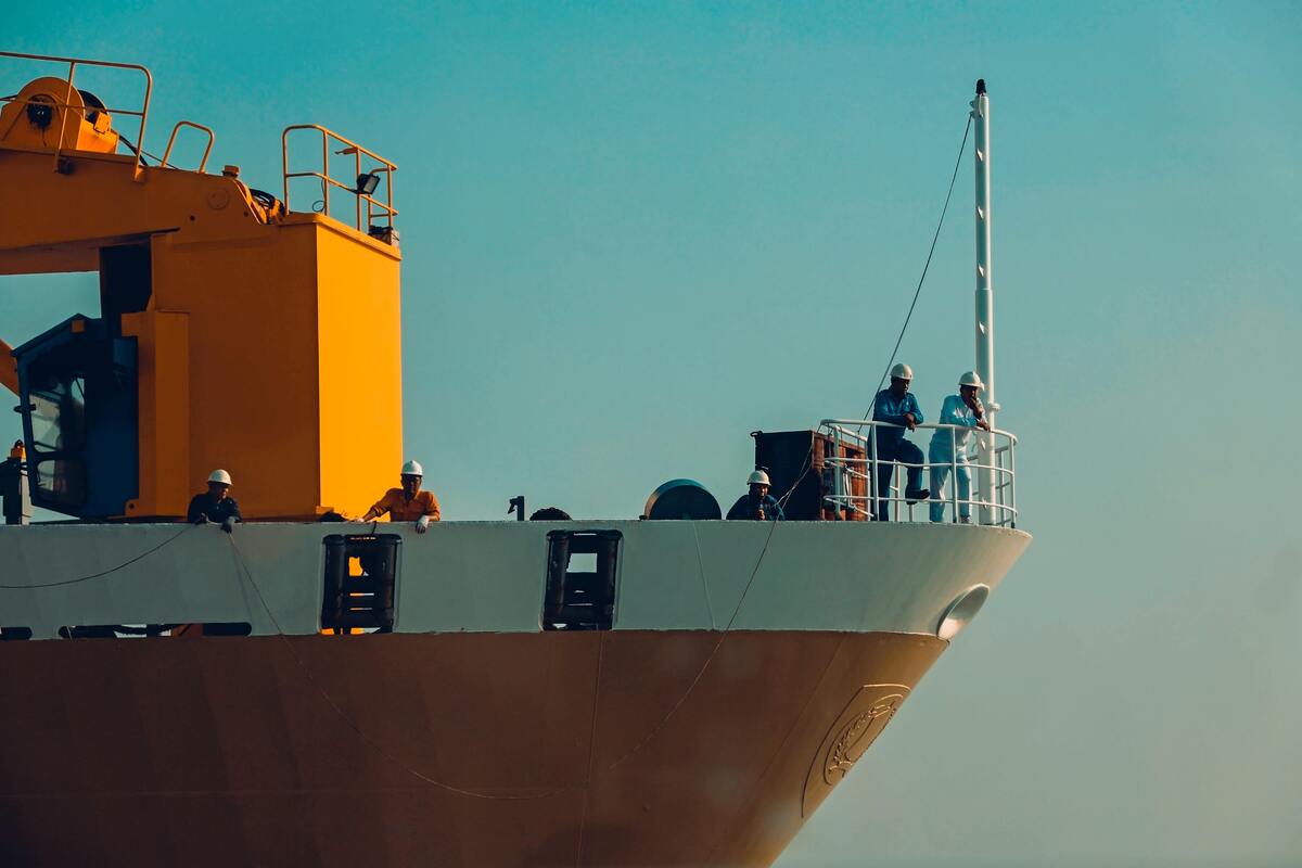 Parte frontal de um navio, pessoas dentro dele usando capacete. 