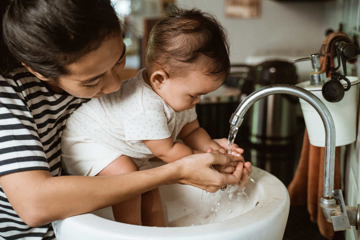 Mamãe lavando as mãos do bebe na torneira 