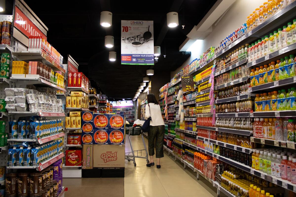 Uma mulher pegando coisas na prateleira de um supermercado. 