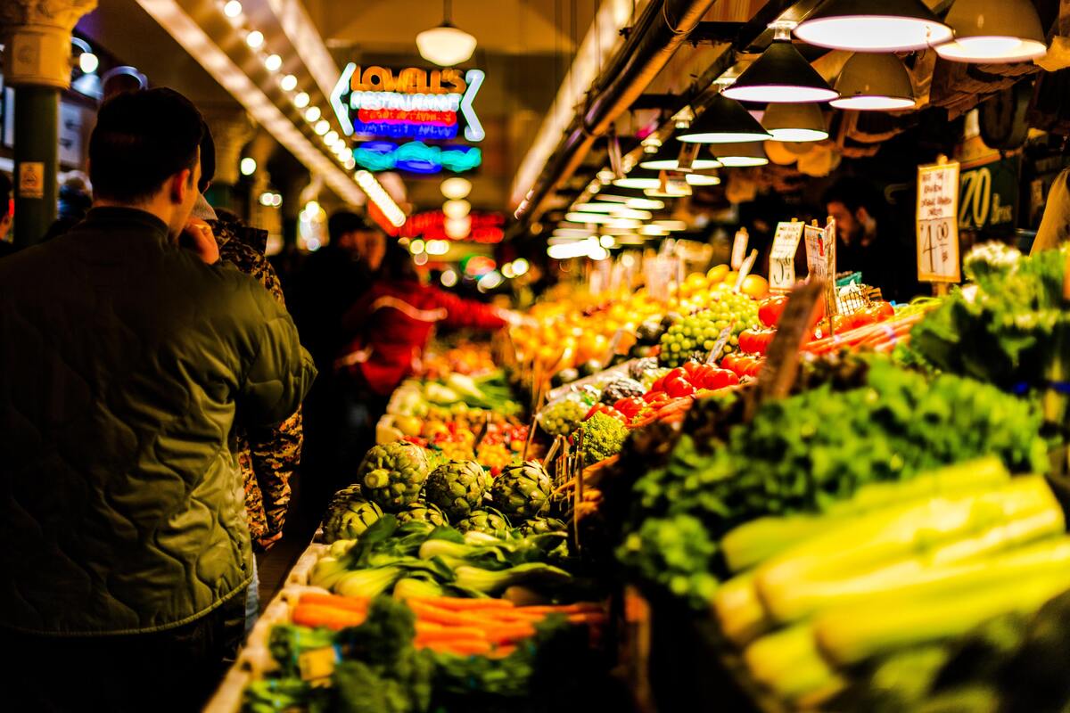 Seção de frutas de um supermercado, algumas pessoas em uma fila. 