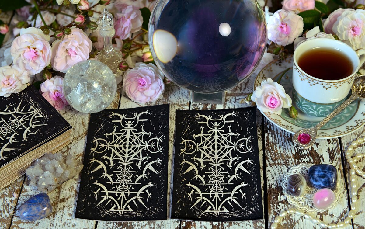 Cartas de Tarot viradas de cabeça para baixo em mesa de madeira com flores e chá.