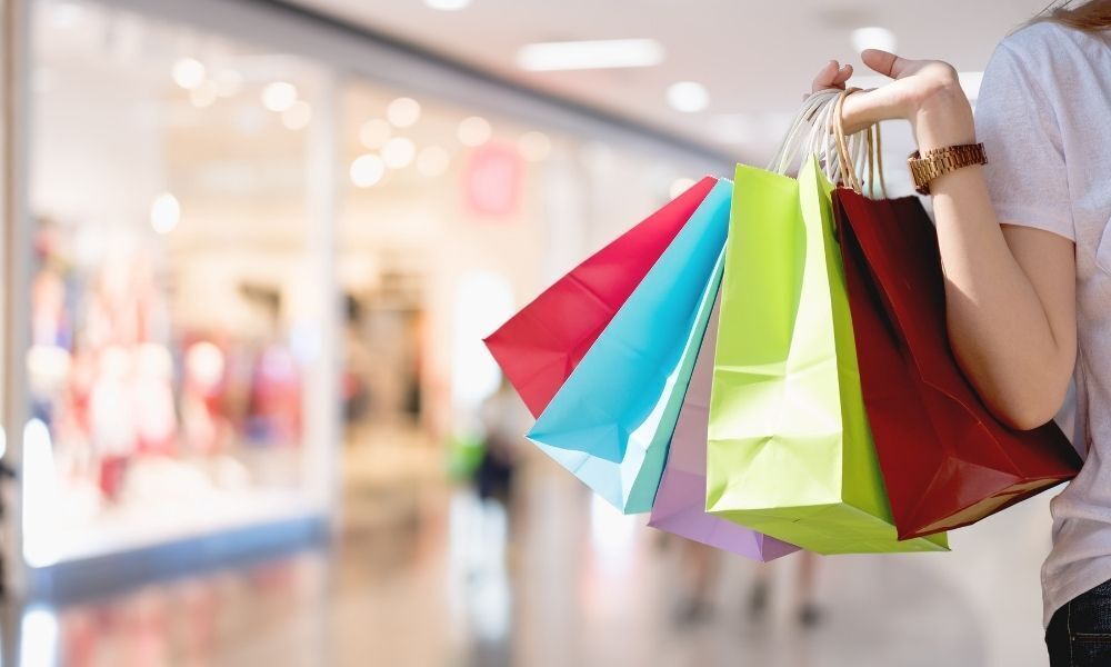 mão carrega sacolas em frente à lojas