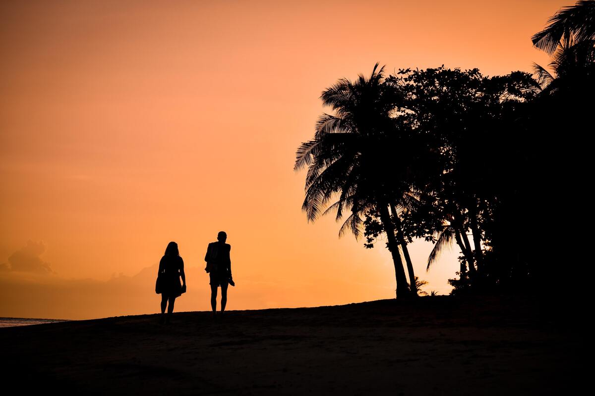 Casal andando lado a lada em uma praia.