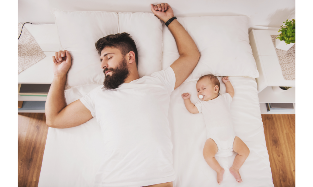 Pai e filha bebê dormindo em uma cama lado a lado.