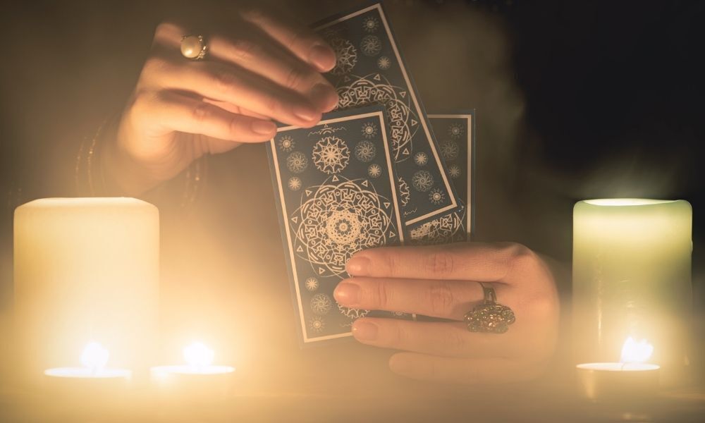 pessoa dispondo cartas de tarot em uma mesa com velas