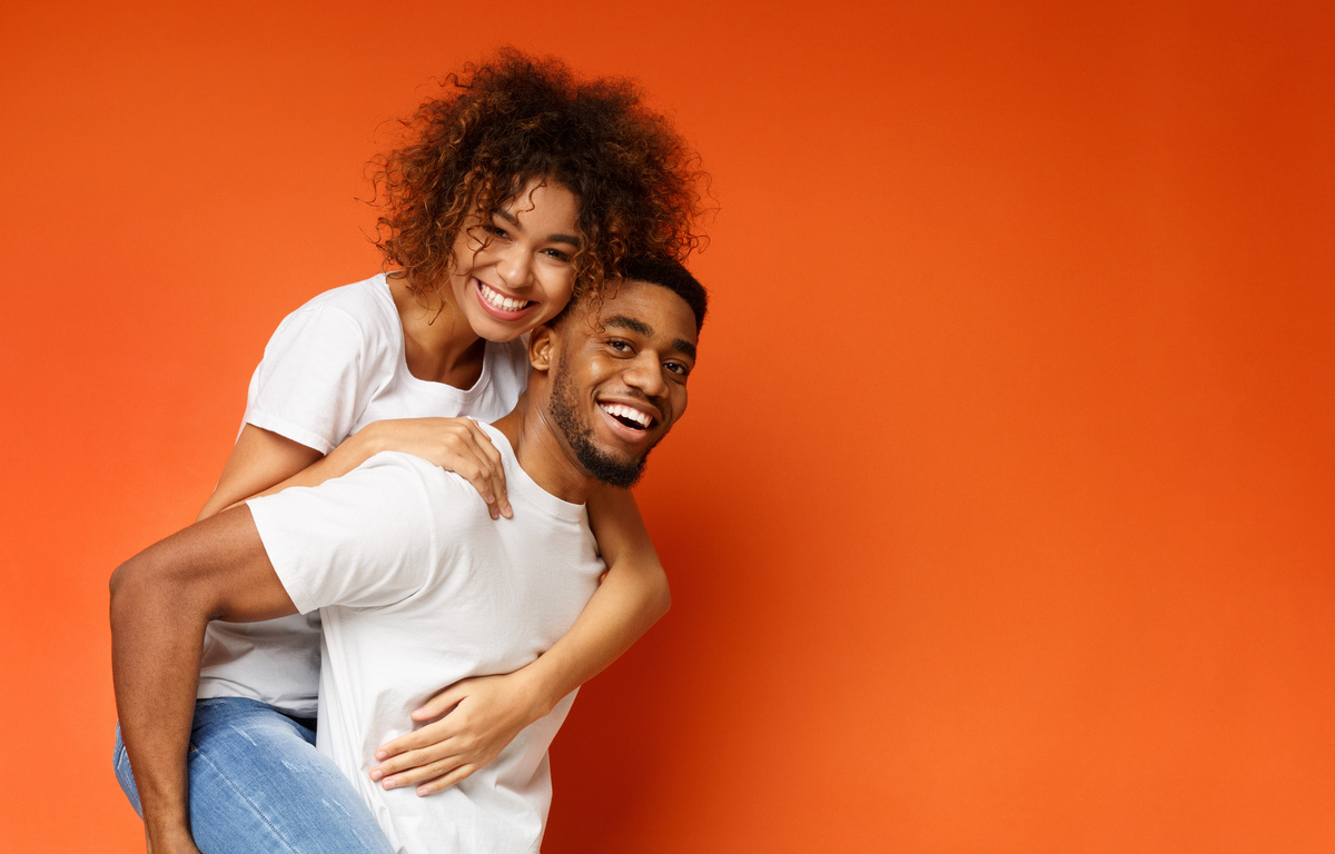 Homem carregando mulher nas costas em fundo laranja