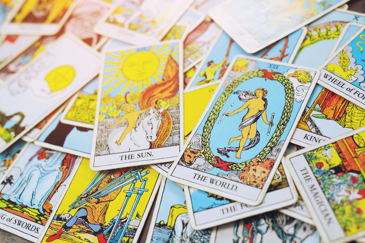 Baralho de tarot espalhado por superfície, com carta mundo e carta sol em evidência.