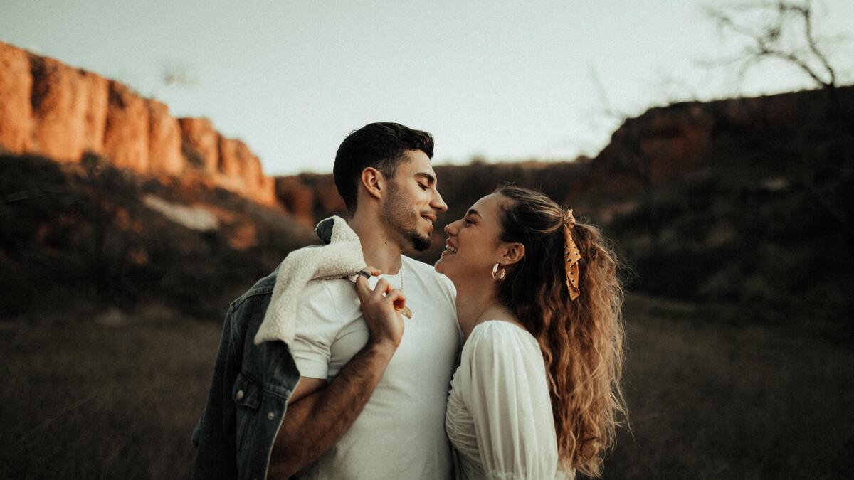 Casal sorrindo juntos, em um campo gramado.