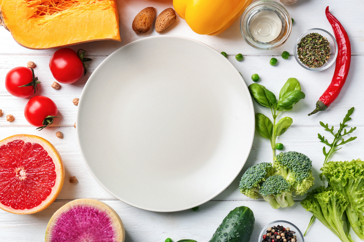 Um prato branco vazio em cima da mesa com frutas e legumes à  sua volta