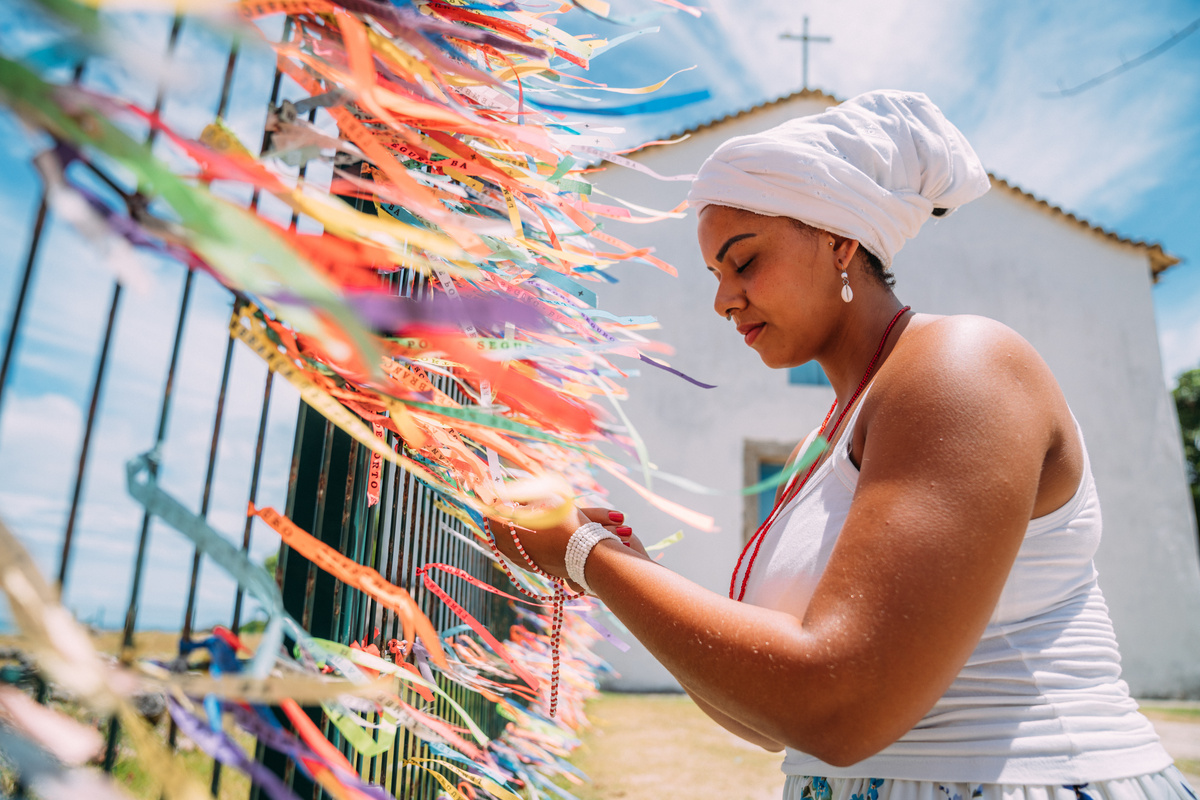 Religiosa da Umbanda amarrando fitinhas do senhor do Bonfim em grade. 