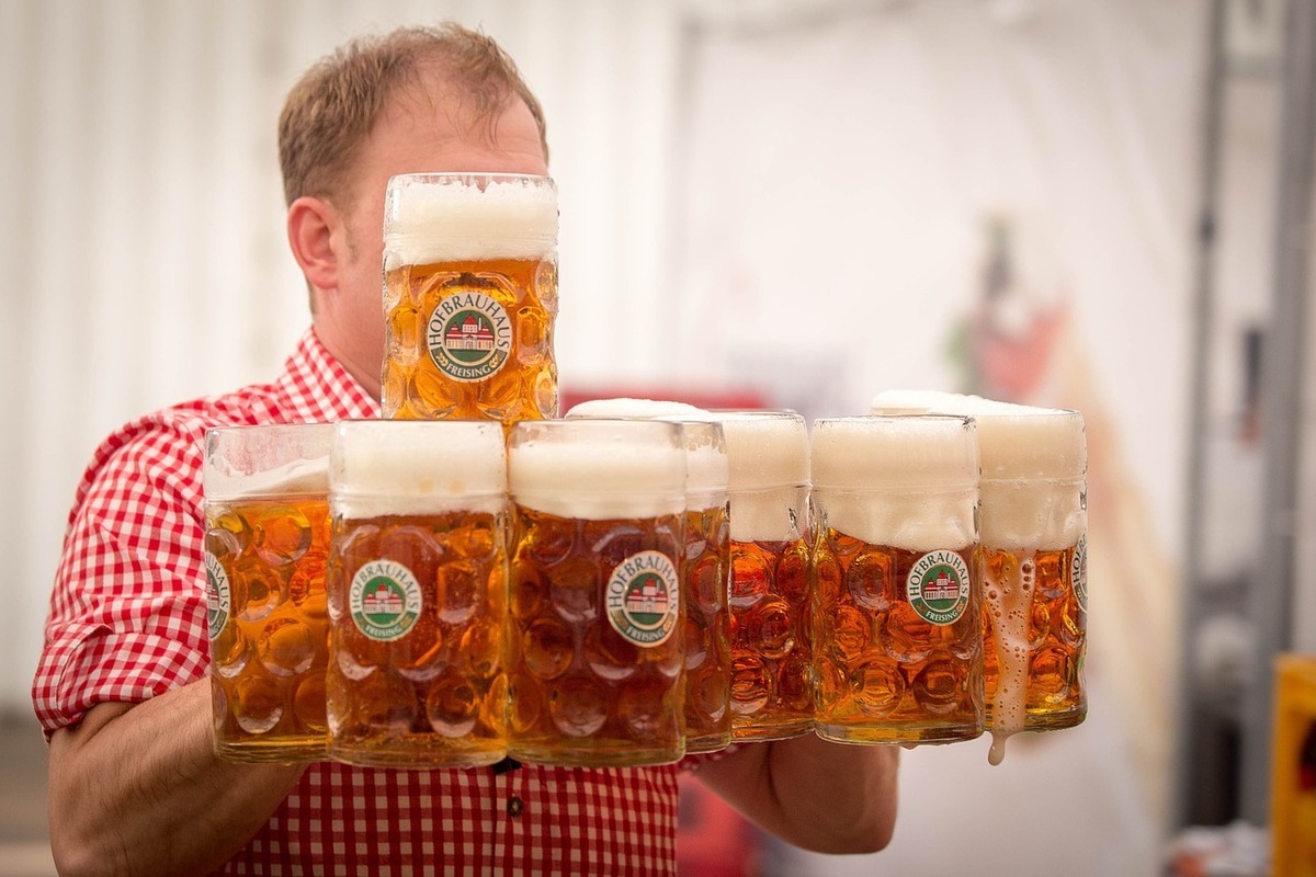 Homem segurando diversos copos de cerveja.