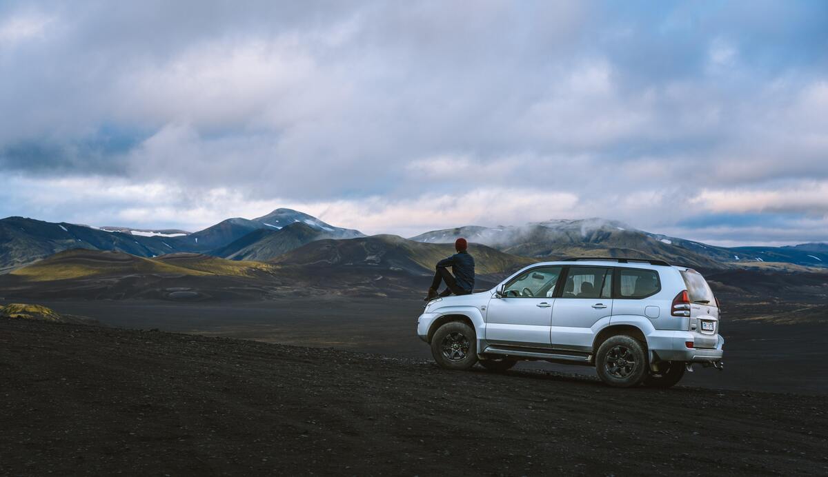 Homem sentado em cima de um carro observando a paisagem