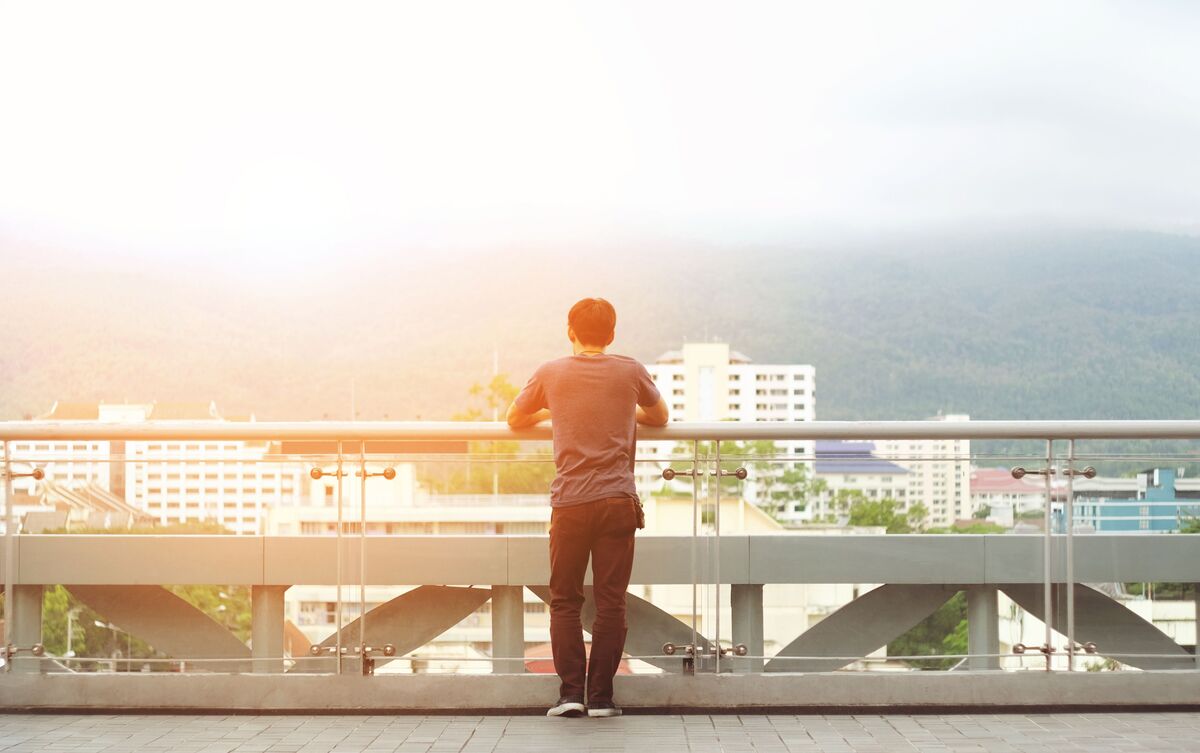 Homem sozinho parado em ponte observando a paisagem.