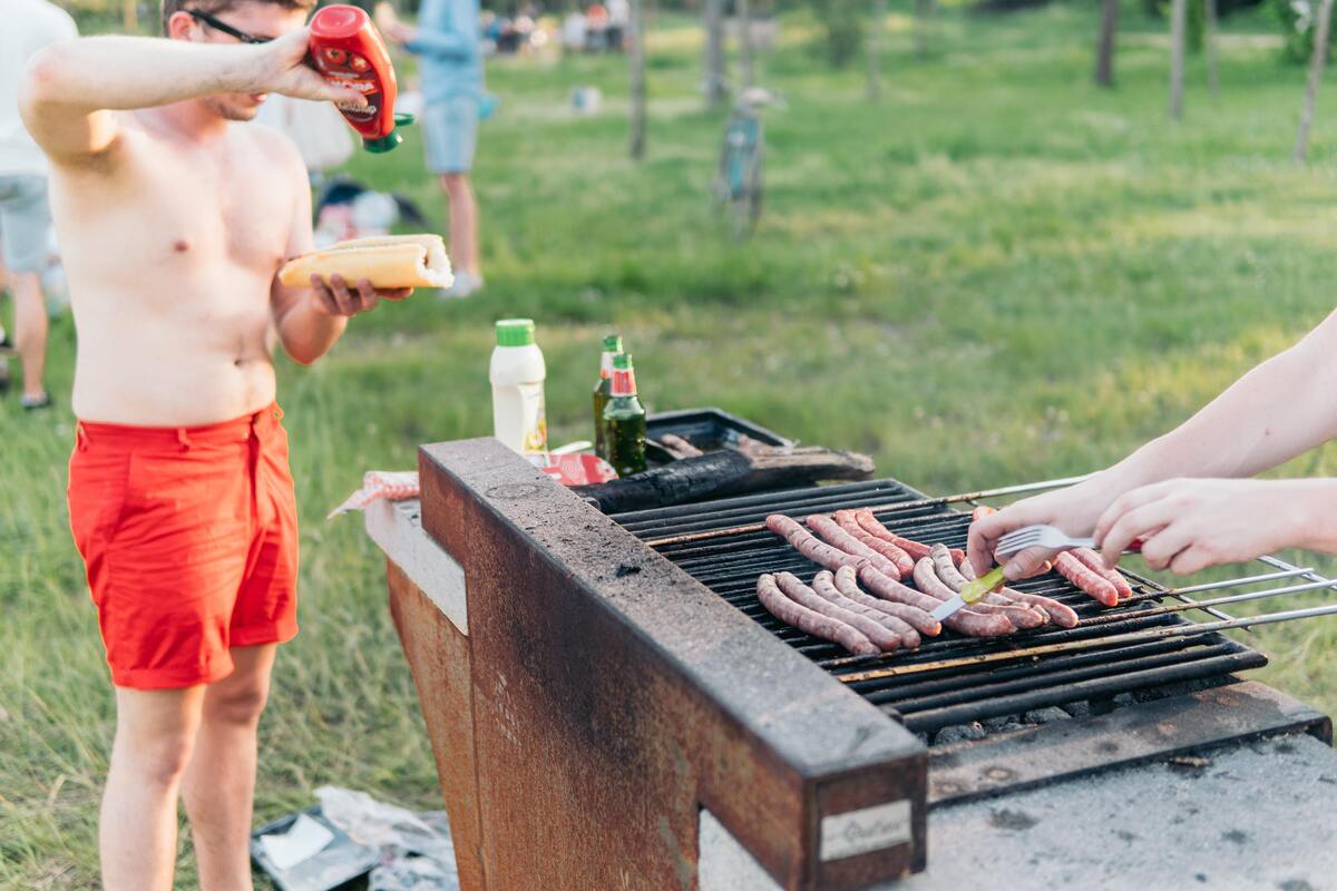 Linguiças na churrasqueira, uma pessoa comendo um cachorro-quente.