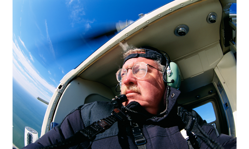 Homem dentro de um helicóptero olhando para o céu ao redor.