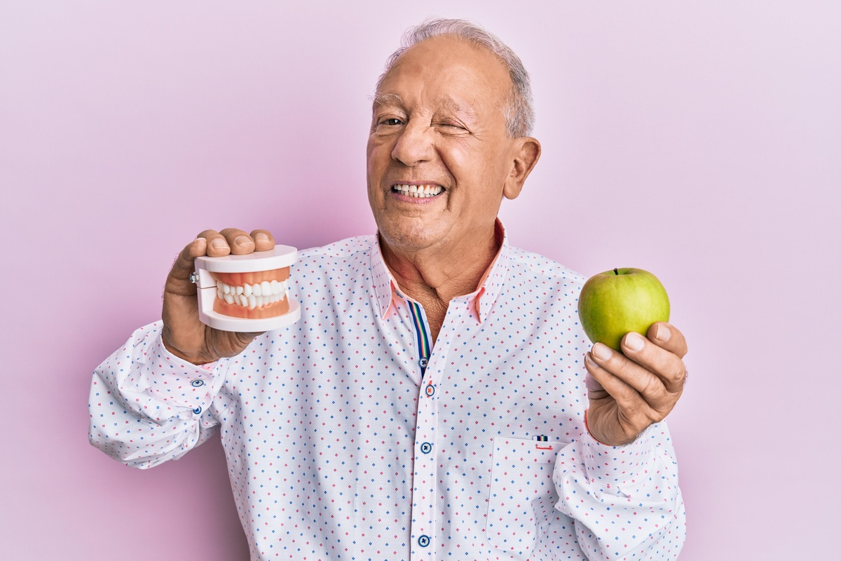 Senhor segurando dentadura e maçã verde