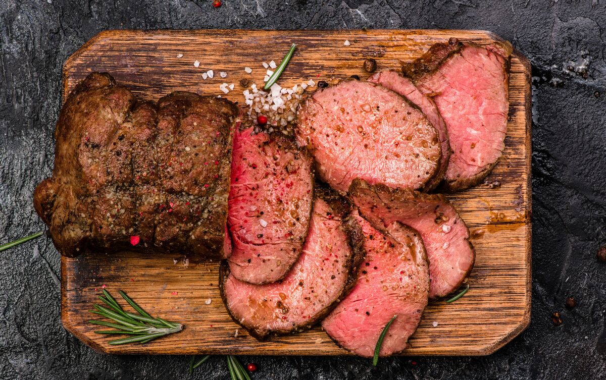 Carne assada sobre bandeja de madeira.