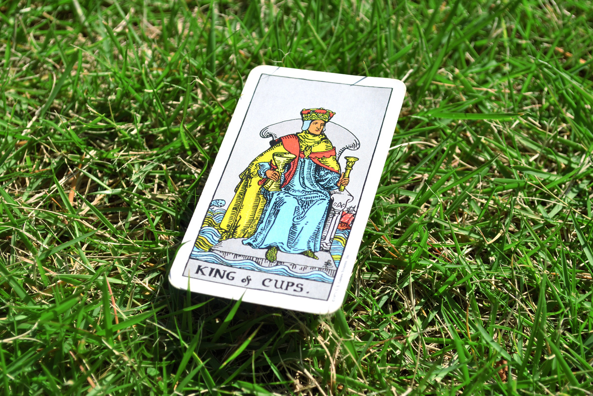 Carta "king of cups" (rei de ouros) em cima de grama