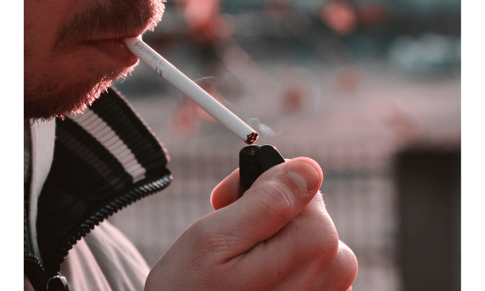 Homem acendendo um cigarro na boca.