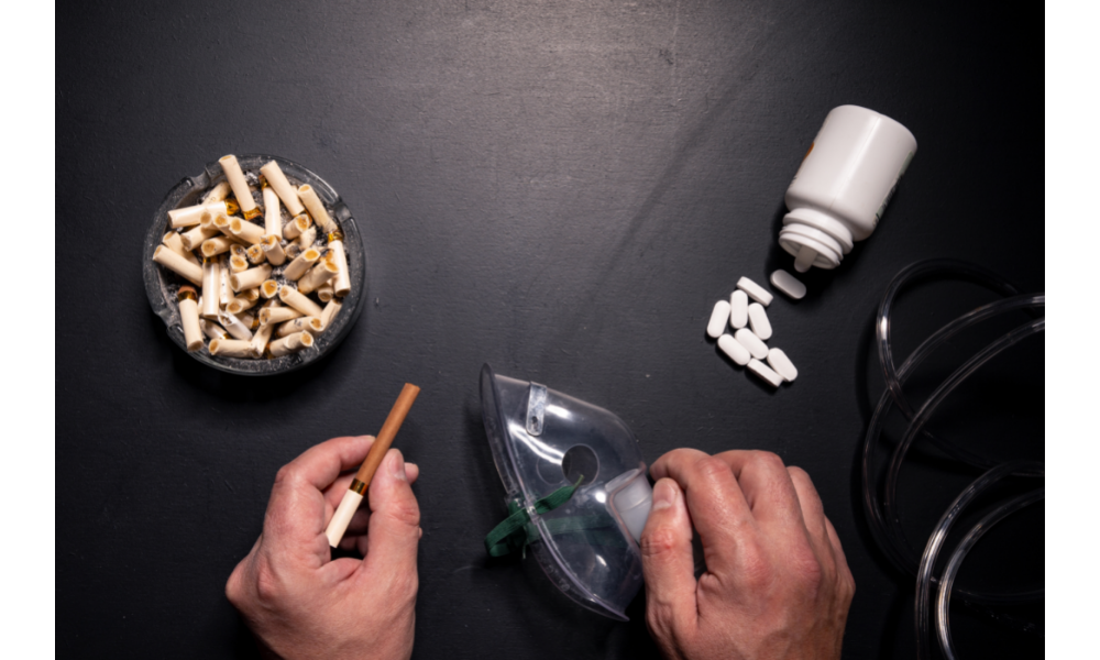 Mãos segurando cigarro em cima de uma mesa preta com vários outros cigarros e um pote de remédios.