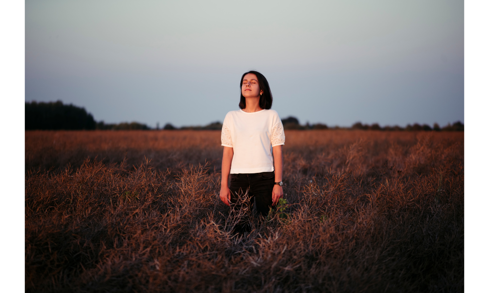 Mulher de olhos fechados em um campo aproveitando o por do sol.