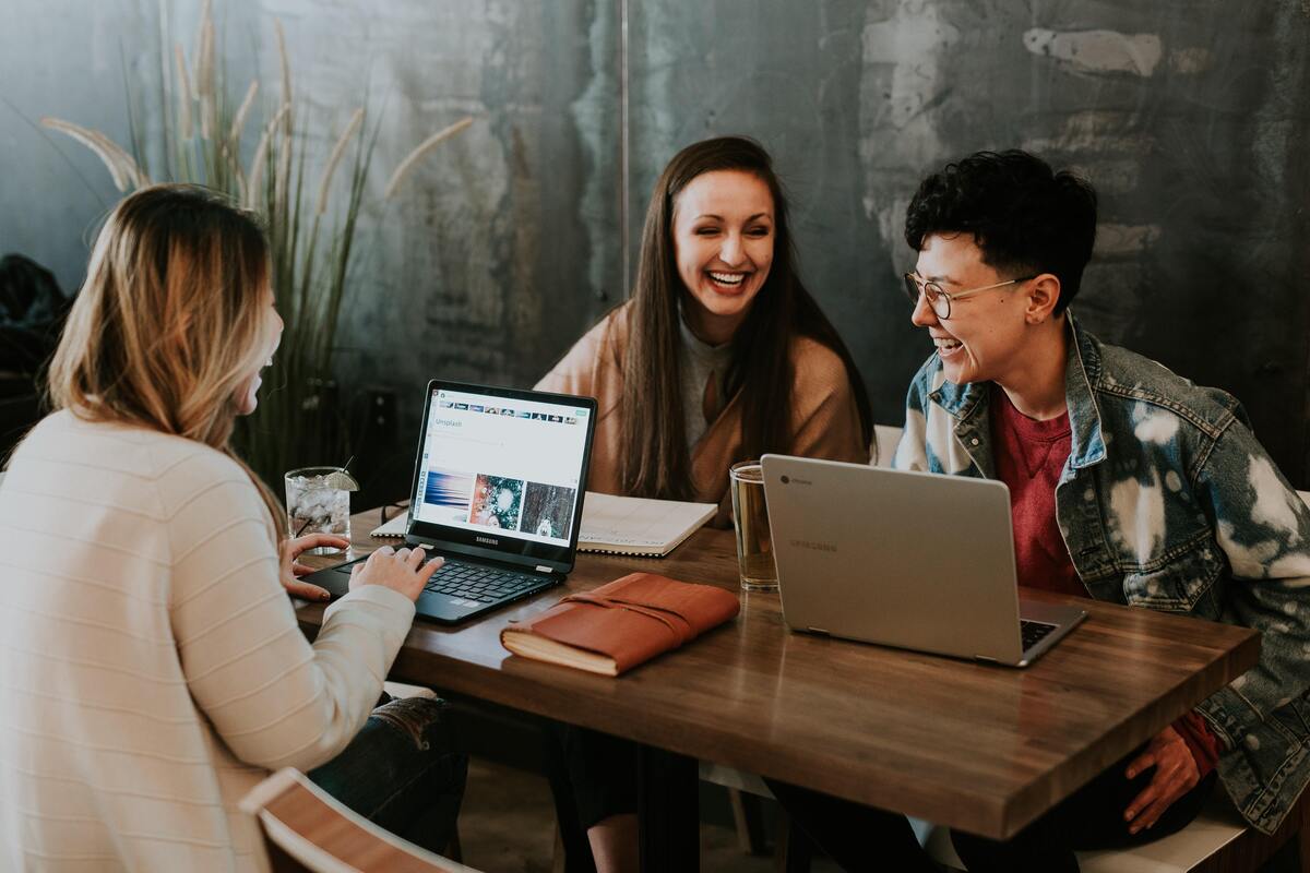 Três pessoas trabalhando com notebooks em uma mesa.