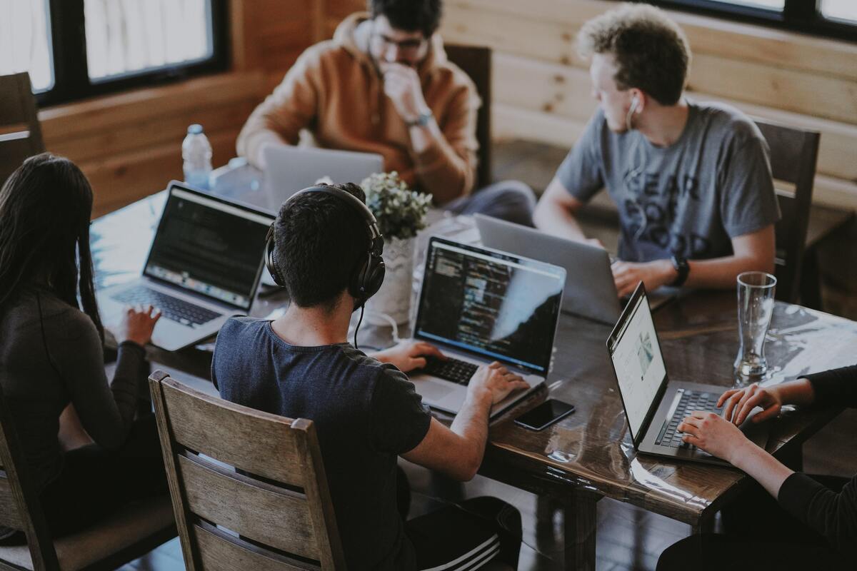 Cinco pessoas em volta de uma mesa trabalhando com notebooks.