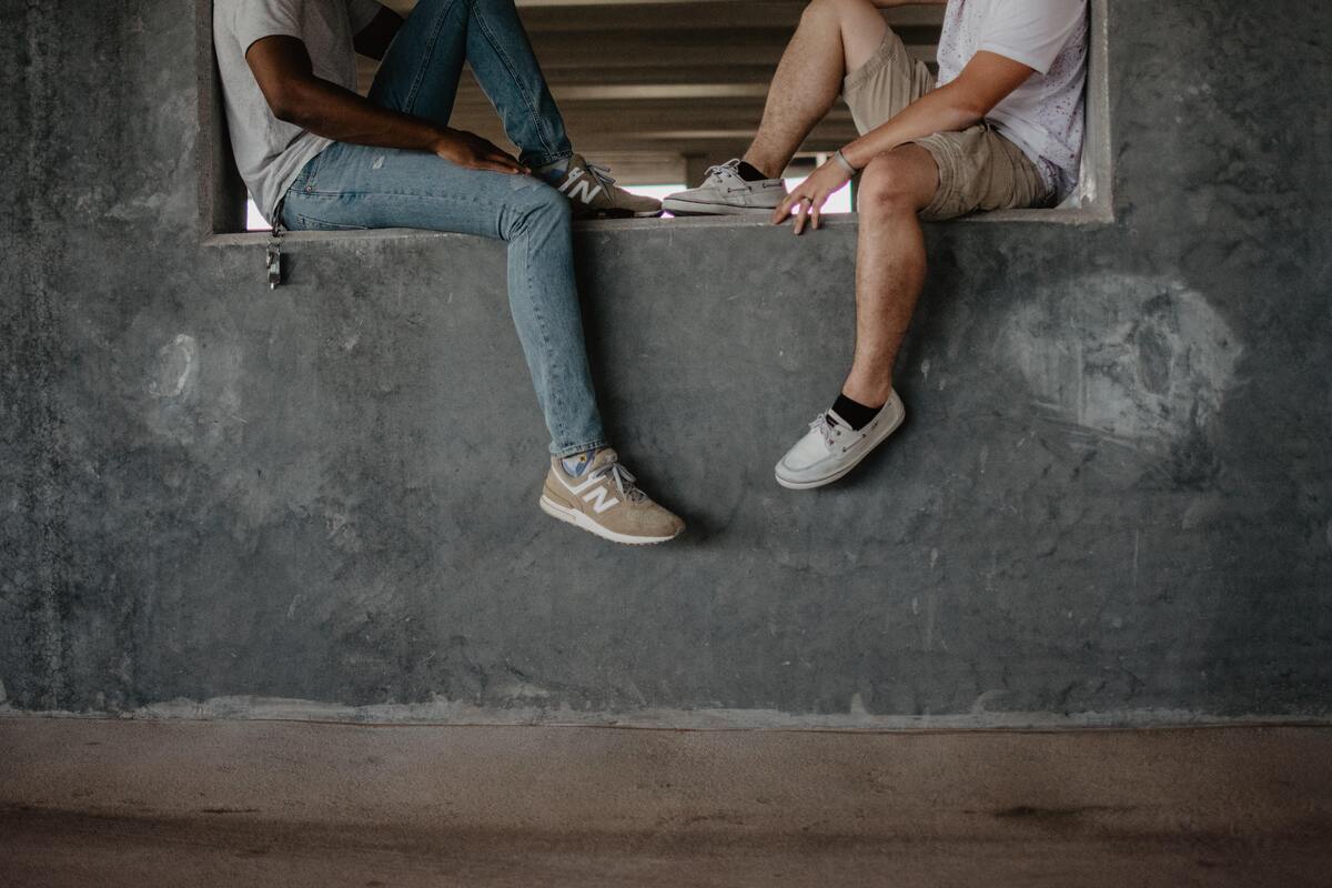 Dois homens sentados em uma janela, com os pés pendurados.