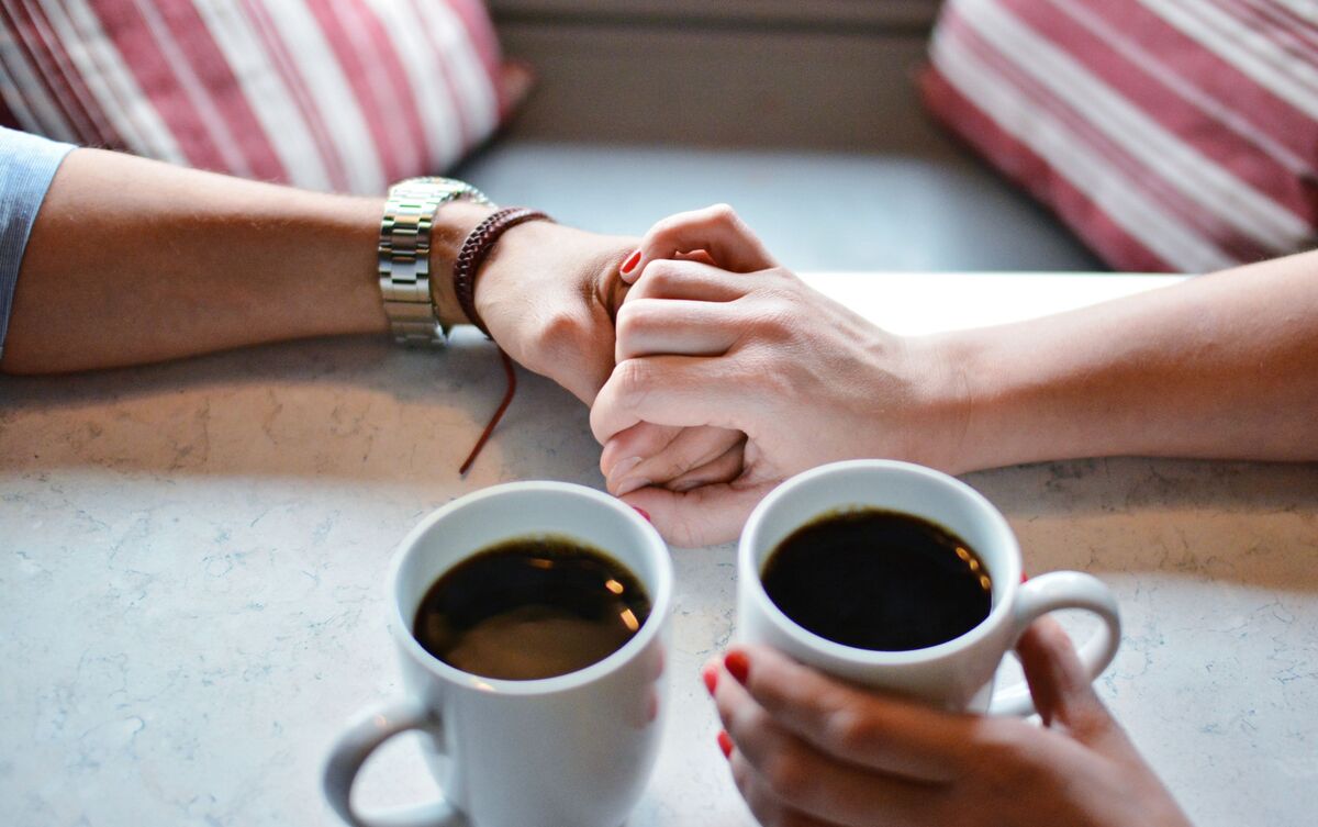 Casal tomando café de mãos dadas.