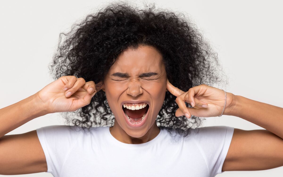 Mulher de olhos fechados e tapando as orelhas.