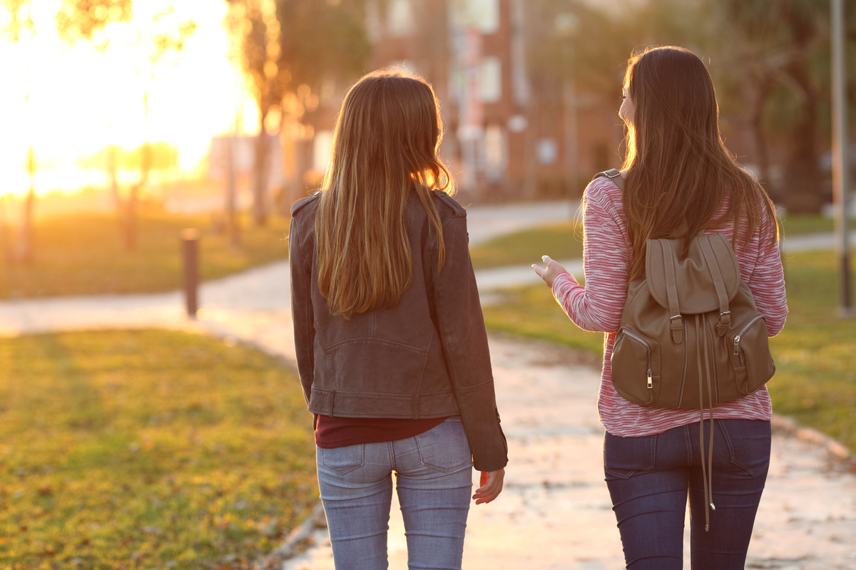 Duas mulheres caminhando juntas em cenário de fim de tarde, enquanto conversam.