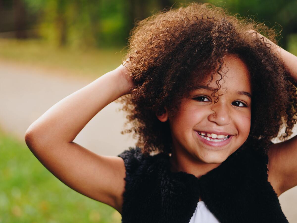 Menina negra sorrindo com as mãos no cabelo.